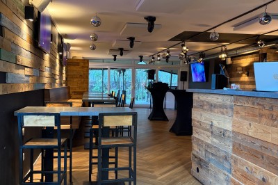 Vue d'un intérieur avec un espace ouvert, un bar en briques, un parquet clair et une mezzanine avec rambarde blanche.
