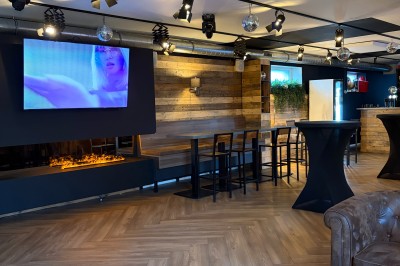 Vue d'un intérieur avec un espace ouvert, un bar en briques, un parquet clair et une mezzanine avec rambarde blanche.