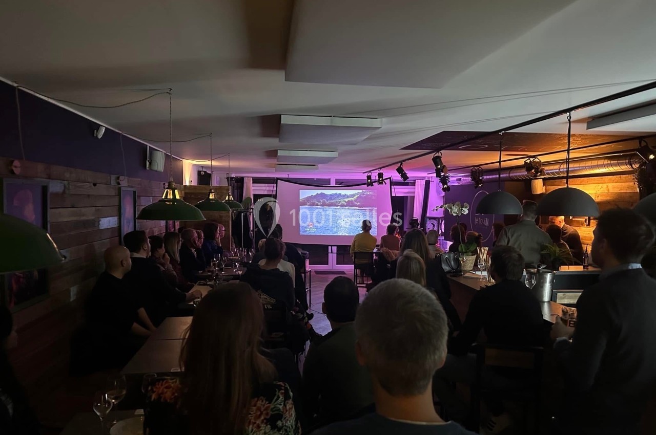 Un groupe de personnes assises dans un bar sombre regarde une projection sur un écran.