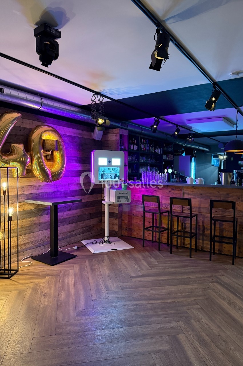 Bar moderne avec comptoir en bois, tabourets, décor lumineux et ballons dorés formant le chiffre 40.