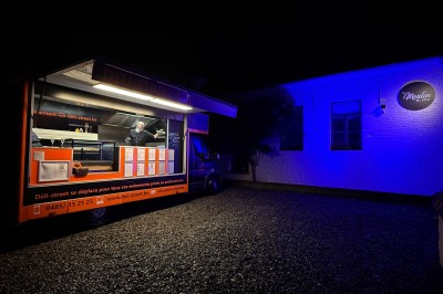 Camion de restauration éclairé la nuit, stationné devant un bâtiment illuminé par une lumière bleue.