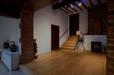 Salle lumineuse avec parquet clair, table et chaises au centre, escalier blanc, machine à coudre ancienne et tableau au mur.