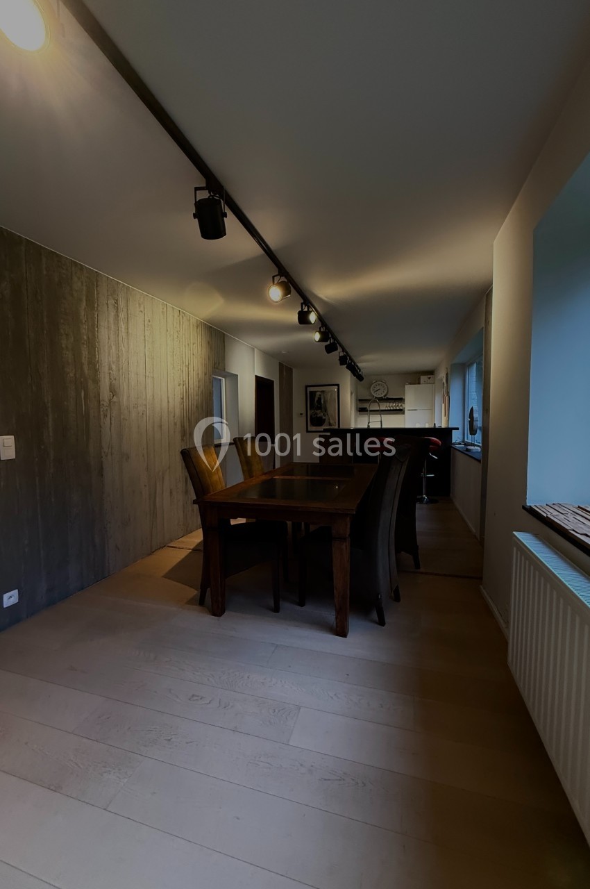 Salle à manger avec table en bois, chaises rembourrées, mur texturé et éclairage sur rail au plafond.