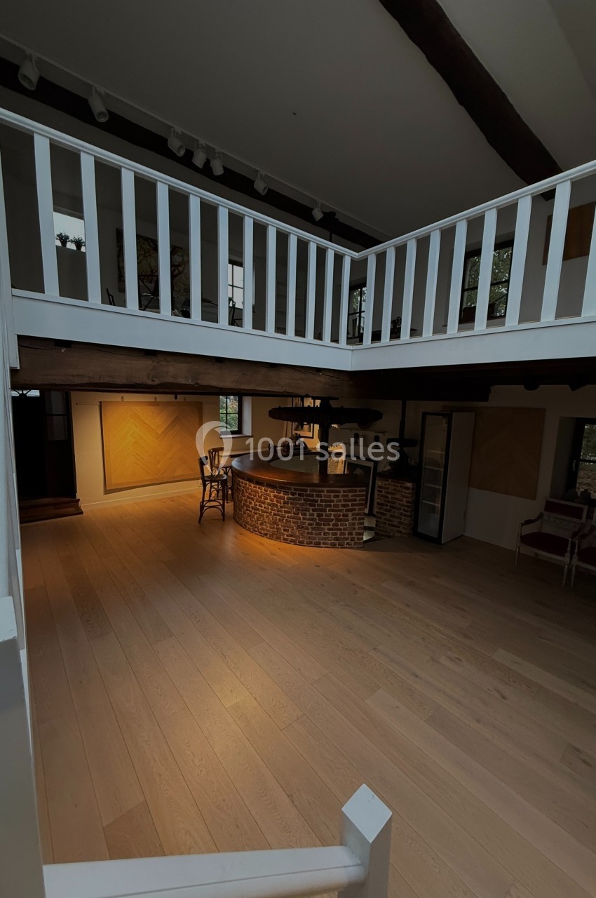 Vue d'un intérieur spacieux avec un sol en bois clair, une mezzanine blanche et un bar en briques éclairé.