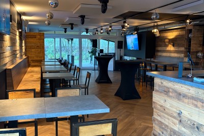 Salle lumineuse avec parquet clair, table et chaises au centre, escalier blanc, machine à coudre ancienne et tableau au mur.