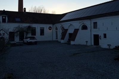 Salle lumineuse avec parquet clair, table et chaises au centre, escalier blanc, machine à coudre ancienne et tableau au mur.