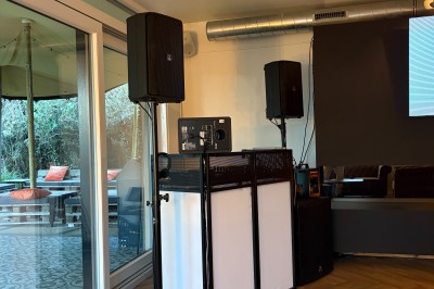 Salle lumineuse avec parquet clair, table et chaises au centre, escalier blanc, machine à coudre ancienne et tableau au mur.