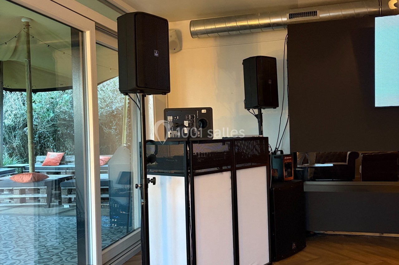 Équipement de sonorisation installé dans une salle, avec enceintes, table de mixage et vue partielle sur une terrasse…