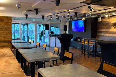 Salle lumineuse avec parquet clair, table et chaises au centre, escalier blanc, machine à coudre ancienne et tableau au mur.