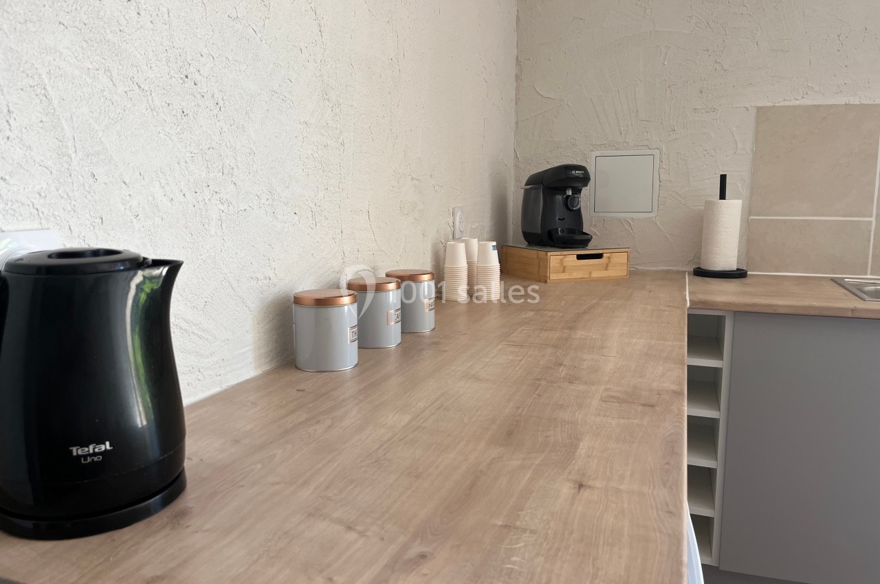 Plan de travail en bois avec bouilloire, pots de rangement, machine à café, gobelets et porte-essuie-tout.