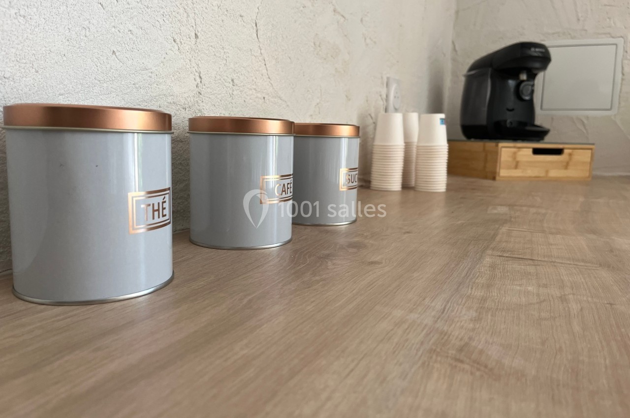 Boîtes de thé et café alignées sur un plan de travail en bois, avec une machine à café et des gobelets en arrière-plan.