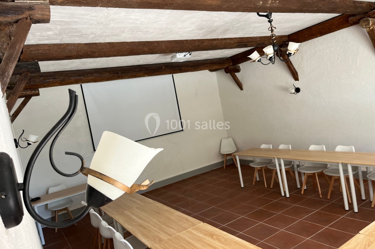 Salle de réunion avec poutres apparentes, tables en bois, chaises blanches et écran de projection mural.