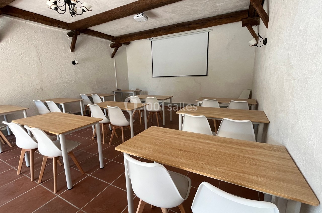 Salle de formation avec des tables en bois clair, chaises blanches, projecteur et écran mural.