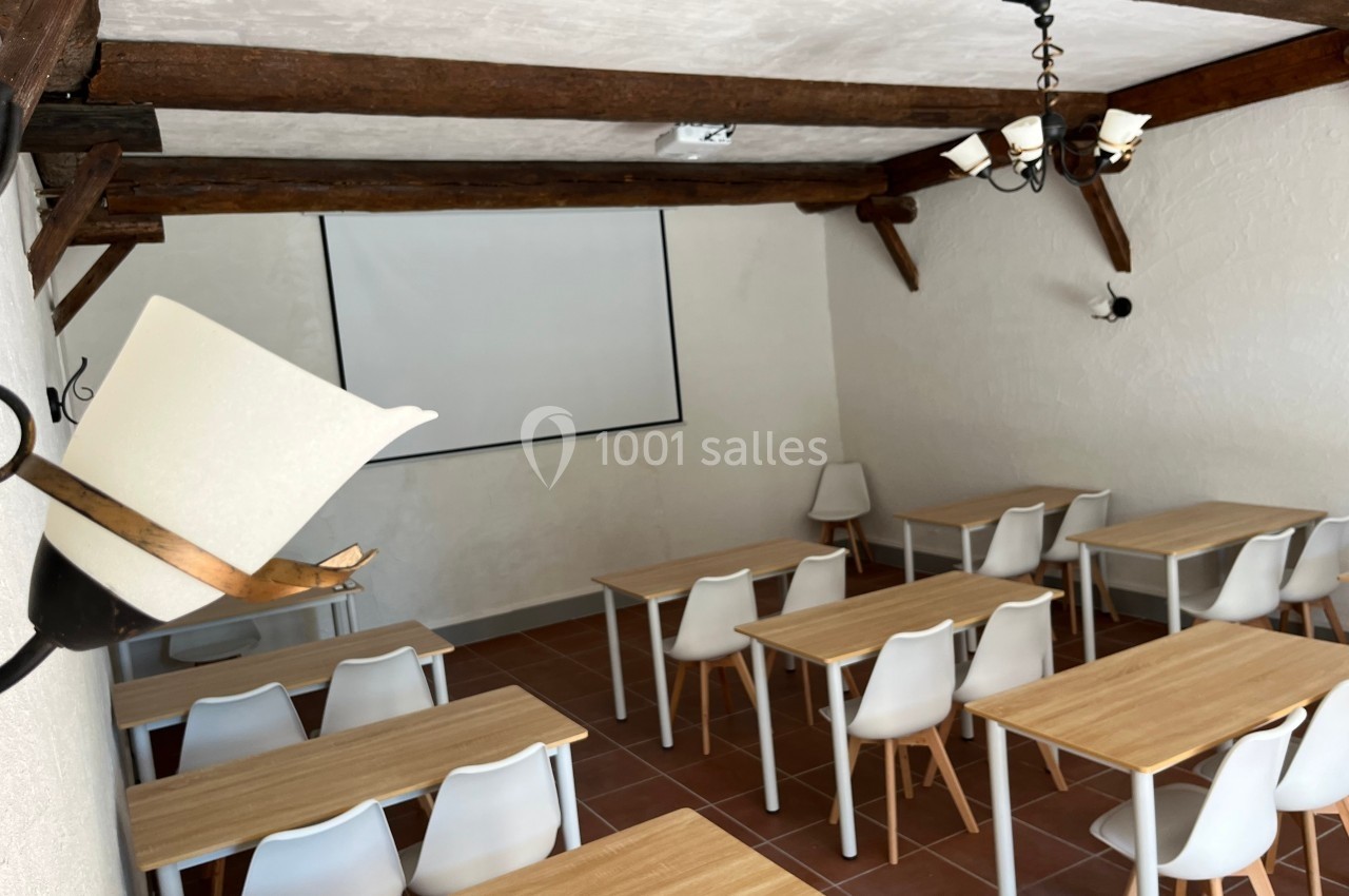 Salle de réunion avec tables en bois, chaises blanches et un écran de projection fixé au mur.