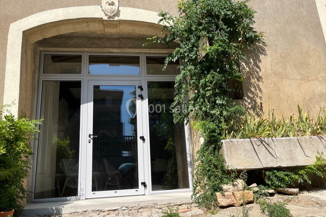 Porte-fenêtre vitrée blanche encadrée de pierre, avec une plante grimpante et une jardinière en pierre à droite.