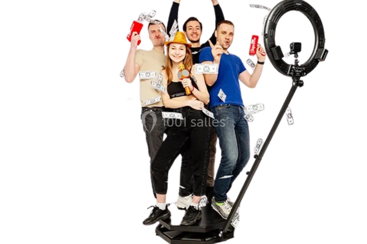 Quatre personnes souriantes posent sur une plateforme avec des accessoires festifs, entourées de faux billets et un anneau…
