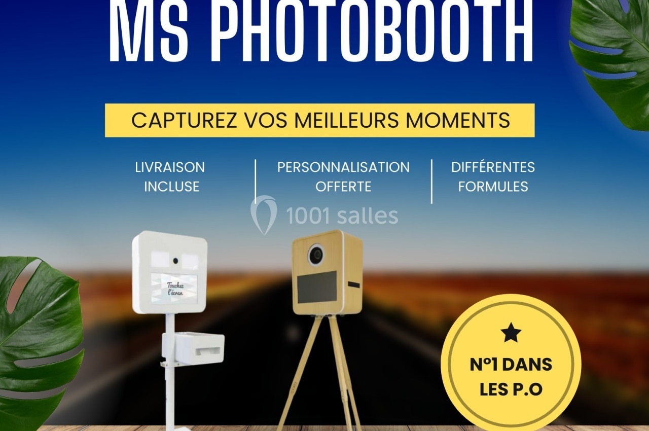 Deux bornes photo sur pied devant une route, avec des textes promotionnels et des feuilles tropicales en décoration.