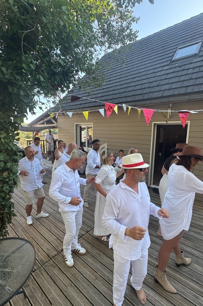 Personnes en tenue blanche dansant en ligne sur une terrasse en bois, décorée de fanions colorés.