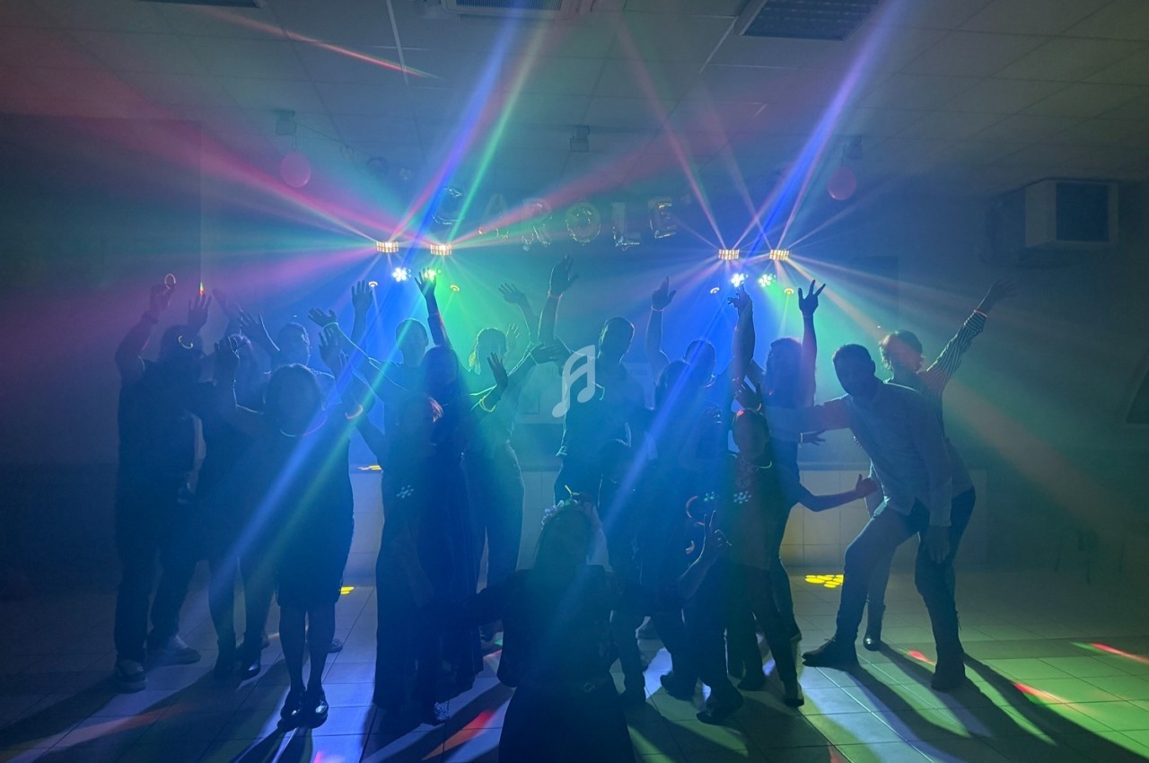 Groupe de personnes dansant sous des lumières colorées dans une salle sombre.