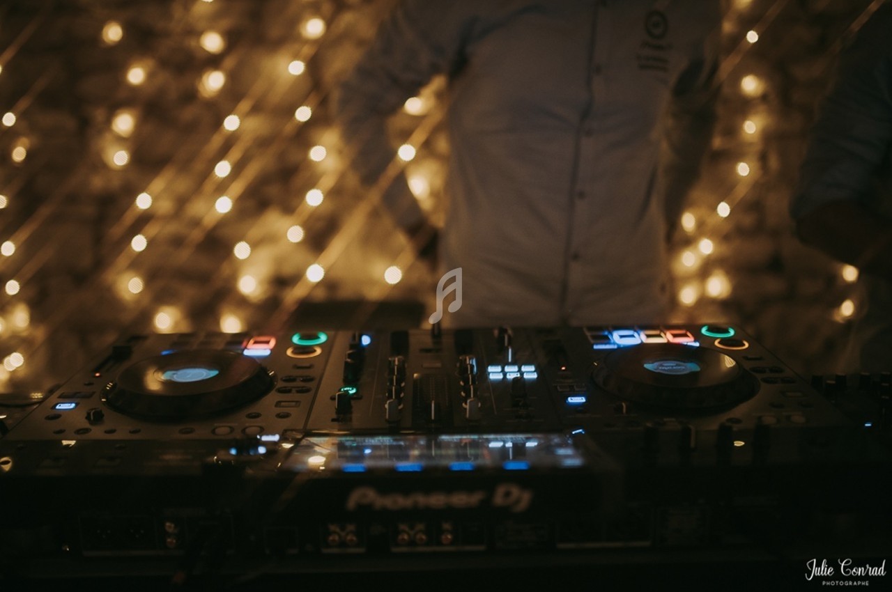 Table de mixage DJ éclairée, avec des lumières floues en arrière-plan et une personne partiellement visible.