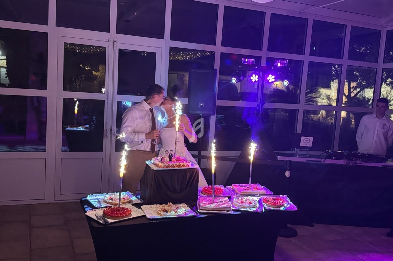 Un couple de mariés partage un moment devant une table garnie de desserts et de fontaines lumineuses.
