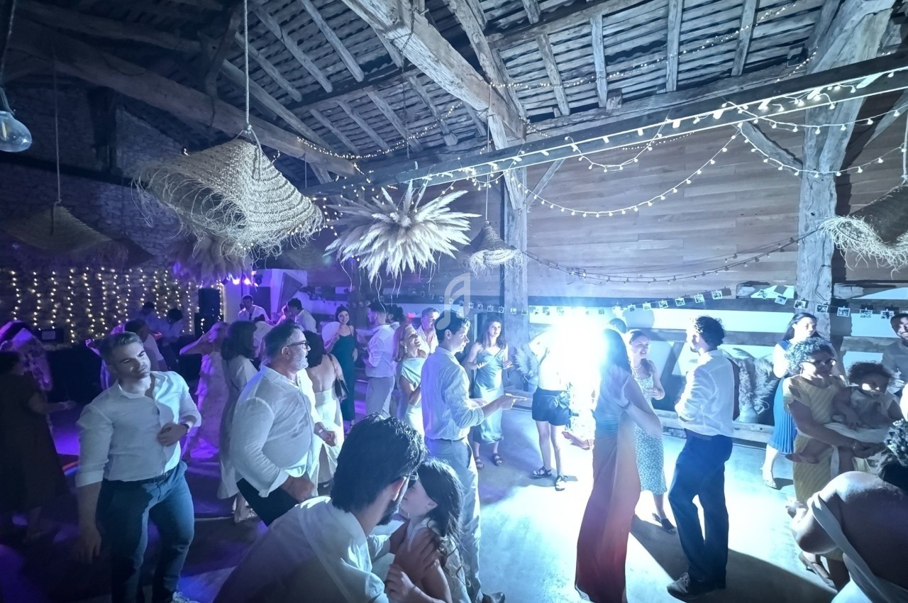 Groupe de personnes dansant dans une grange décorée de guirlandes lumineuses et d'éléments suspendus.