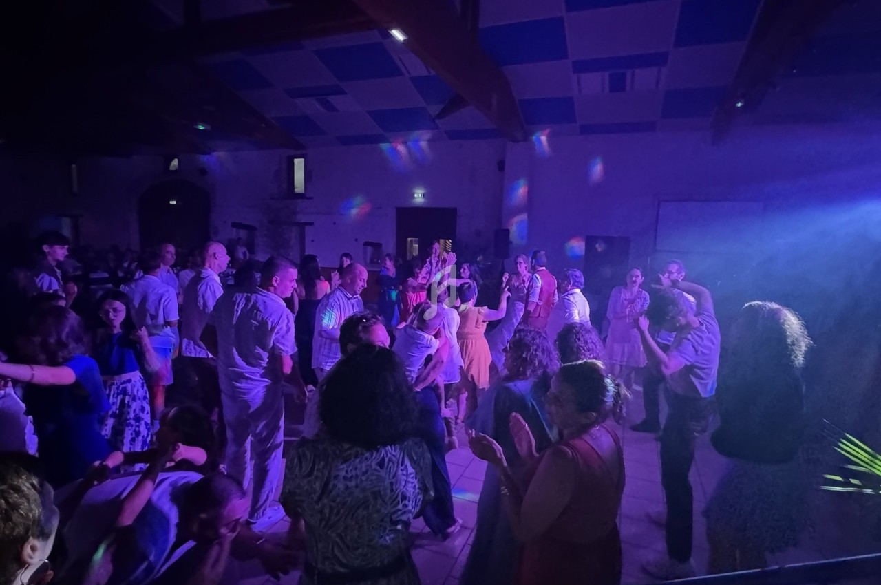 Groupe de personnes dans une salle éclairée par des lumières colorées, dansant et discutant lors d'un événement festif.