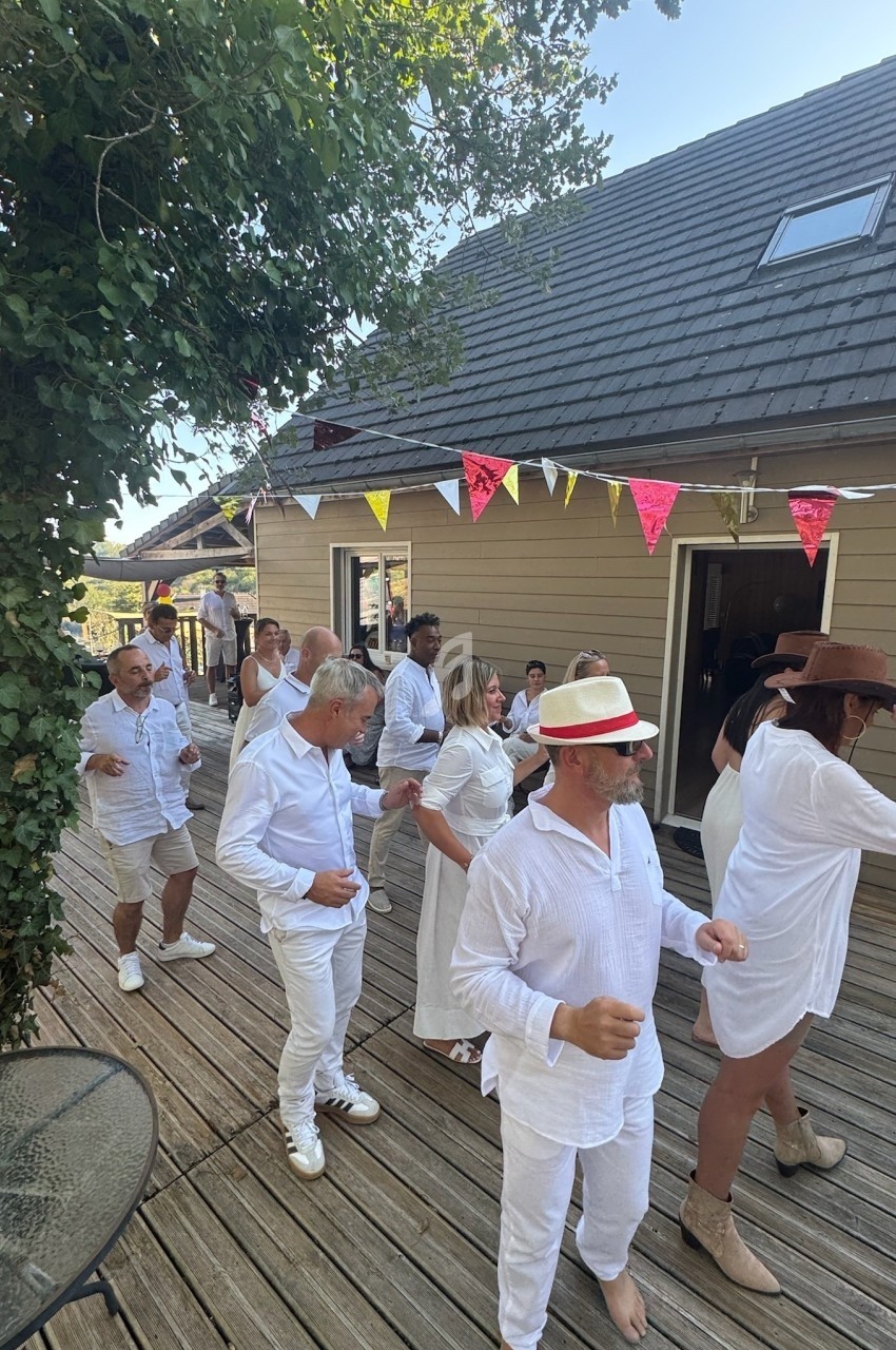 Personnes en tenue blanche dansant en ligne sur une terrasse en bois, décorée de fanions colorés.