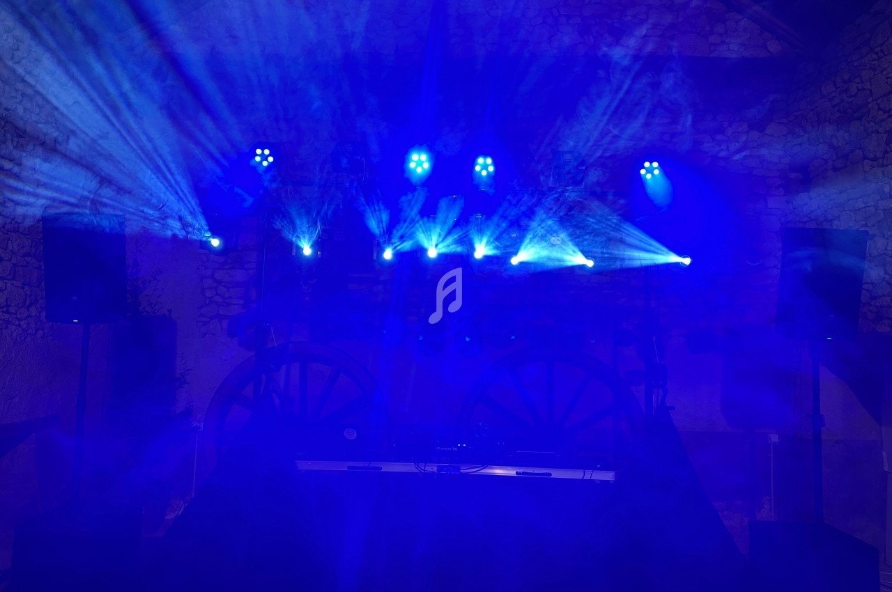 Jeux de lumières bleues projetés dans une salle sombre avec des enceintes et des roues en arrière-plan.