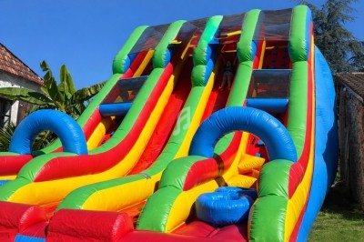 Structure gonflable colorée avec plusieurs toboggans et tunnels, installée sur une pelouse par temps ensoleillé.