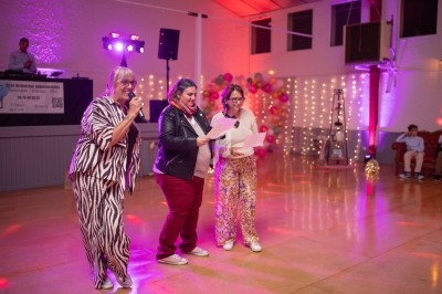 Trois femmes lisent des documents sur une piste de danse éclairée par des lumières colorées lors d'un événement festif.