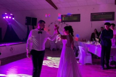 Un couple danse sous des lumières colorées dans une salle de réception avec des invités en arrière-plan.