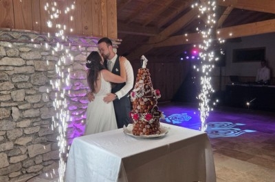 Un couple de mariés s'enlace devant une pièce montée éclairée par des fontaines de lumière dans une salle en bois.