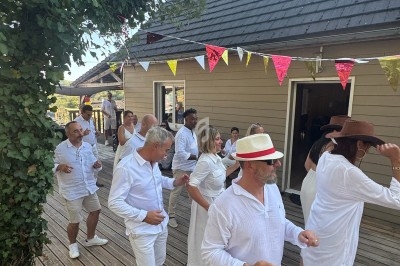 Personnes en tenue blanche dansant en ligne sur une terrasse en bois, décorée de fanions colorés.
