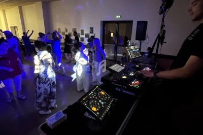 Un DJ anime une soirée dansante dans une salle éclairée par des lumières colorées, avec des participants sur la piste.