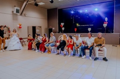 Des personnes assises en ligne dans une salle décorée, avec une scène éclairée et des ballons en arrière-plan.