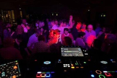 Groupe de personnes dansant dans une salle sombre, éclairée par des lumières colorées, vue depuis une table de mixage.