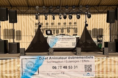 Installation de matériel de sonorisation et éclairage sur une scène extérieure avec une bannière publicitaire au premier…