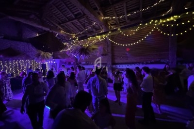 Personnes dansant sous des guirlandes lumineuses dans une salle aux murs en pierre et au plafond en bois.
