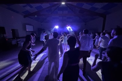 Personnes dansant sous des lumières colorées dans une salle sombre avec un plafond en poutres apparentes.