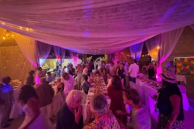 Salle décorée avec des voilages et éclairages colorés, remplie de personnes discutant autour de tables dressées.
