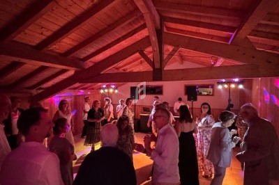 Des personnes dansent dans une salle en bois éclairée par des lumières colorées, créant une ambiance festive.