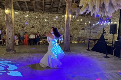 Une mariée danse seule dans une grange éclairée, entourée d'invités assis et de décorations suspendues.