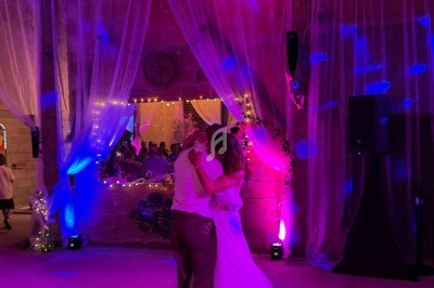 Un couple danse sous des lumières colorées dans une salle décorée de voilages et de guirlandes lumineuses.
