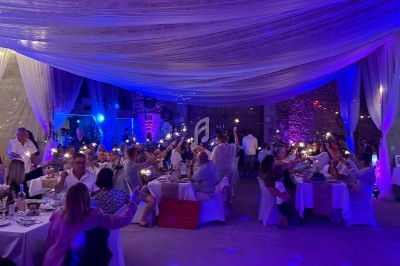 Des invités assis à des tables décorées, levant des lumières dans une salle illuminée de teintes violettes.