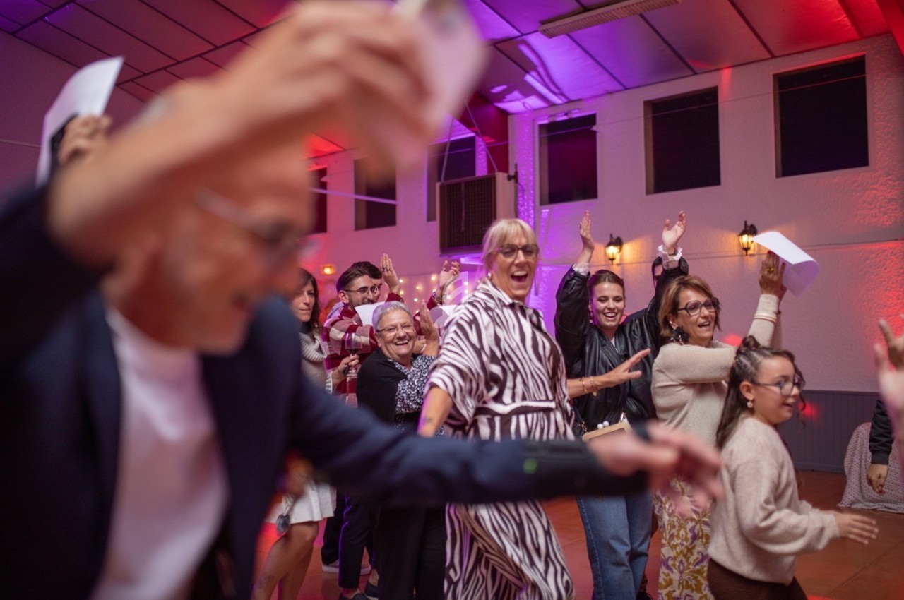 Des personnes de tous âges dansent et s'amusent dans une salle éclairée par des lumières colorées.
