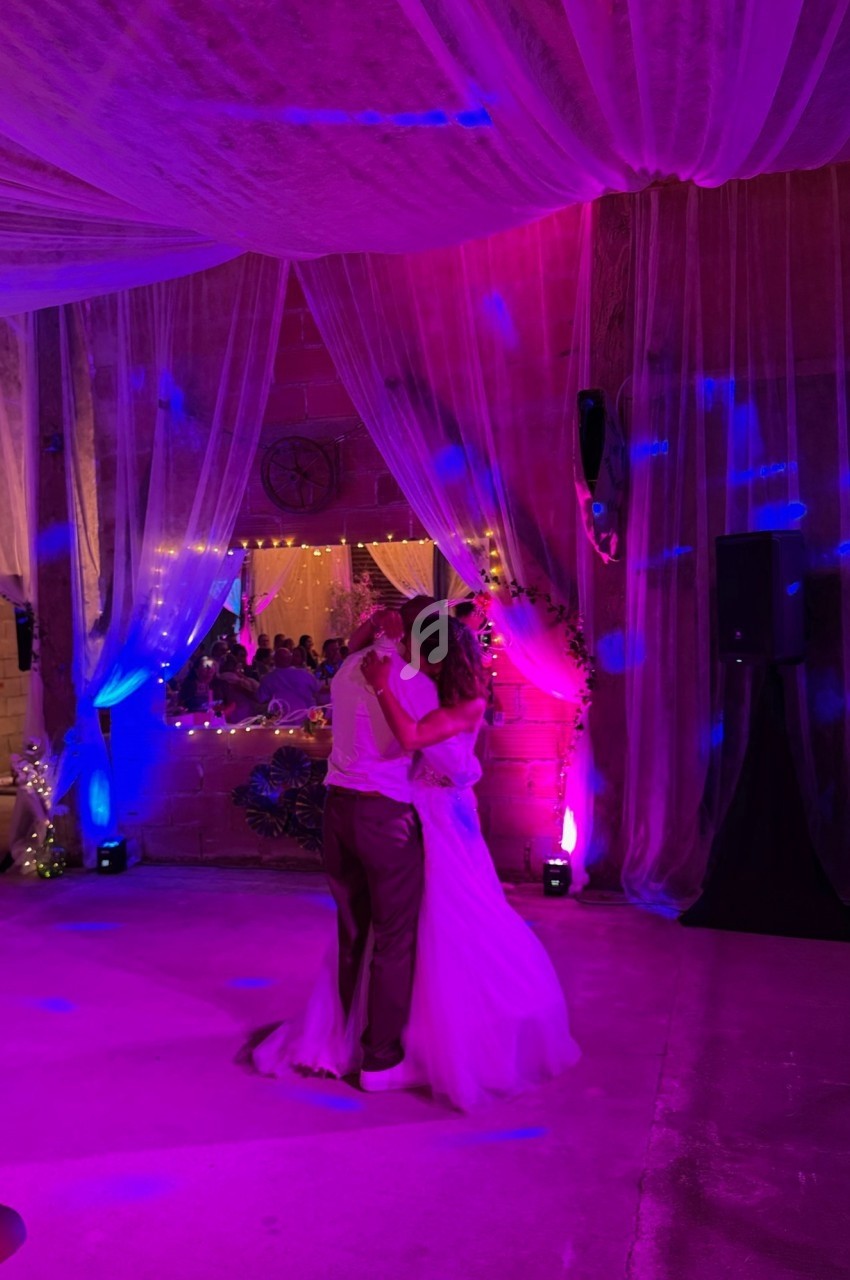 Un couple danse sous des lumières colorées dans une salle décorée de voilages et de guirlandes lumineuses.