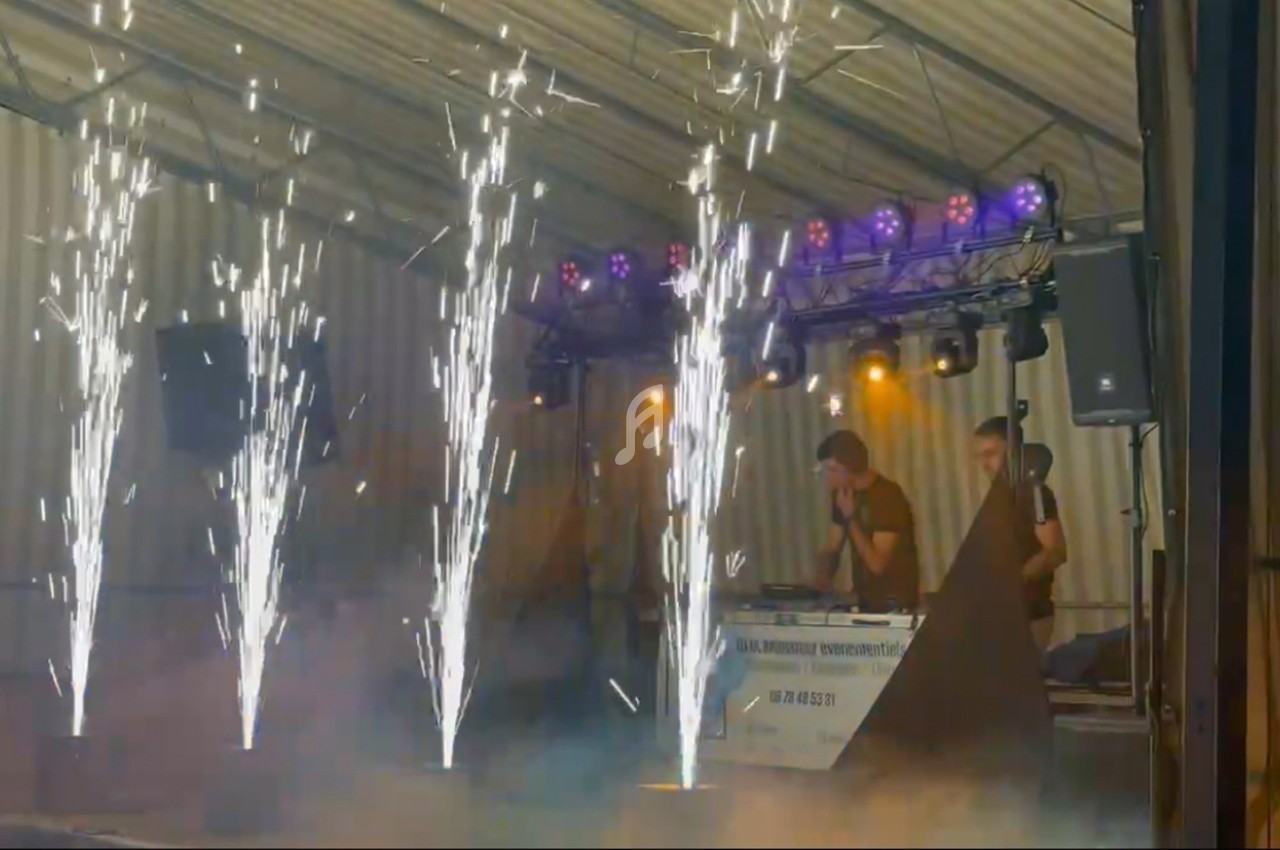 Effets pyrotechniques illuminant une scène avec des DJ en arrière-plan sous un chapiteau.