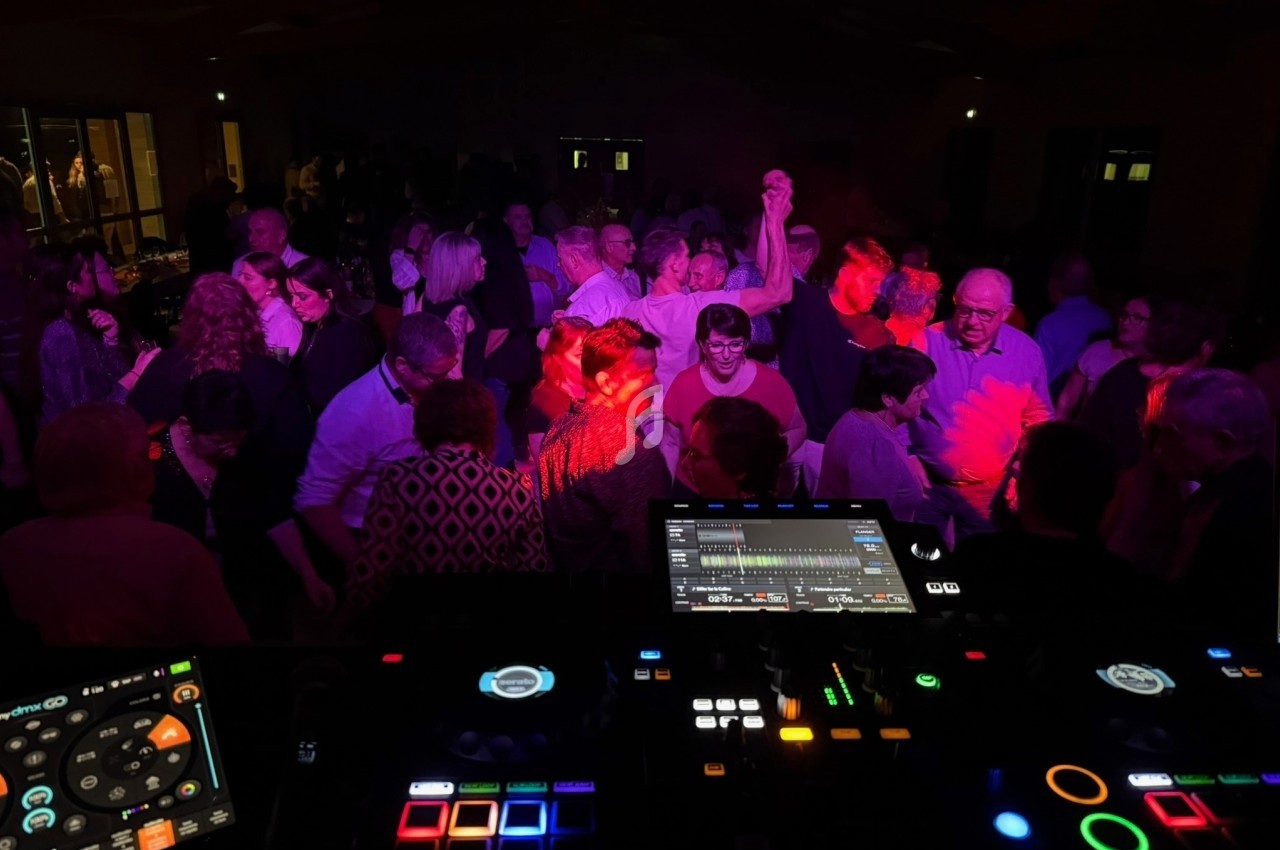 Groupe de personnes dansant dans une salle sombre, éclairée par des lumières colorées, vue depuis une table de mixage.