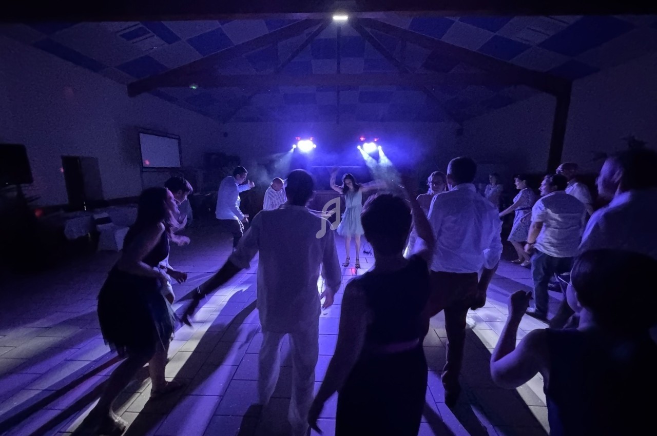 Personnes dansant sous des lumières colorées dans une salle sombre avec un plafond en poutres apparentes.
